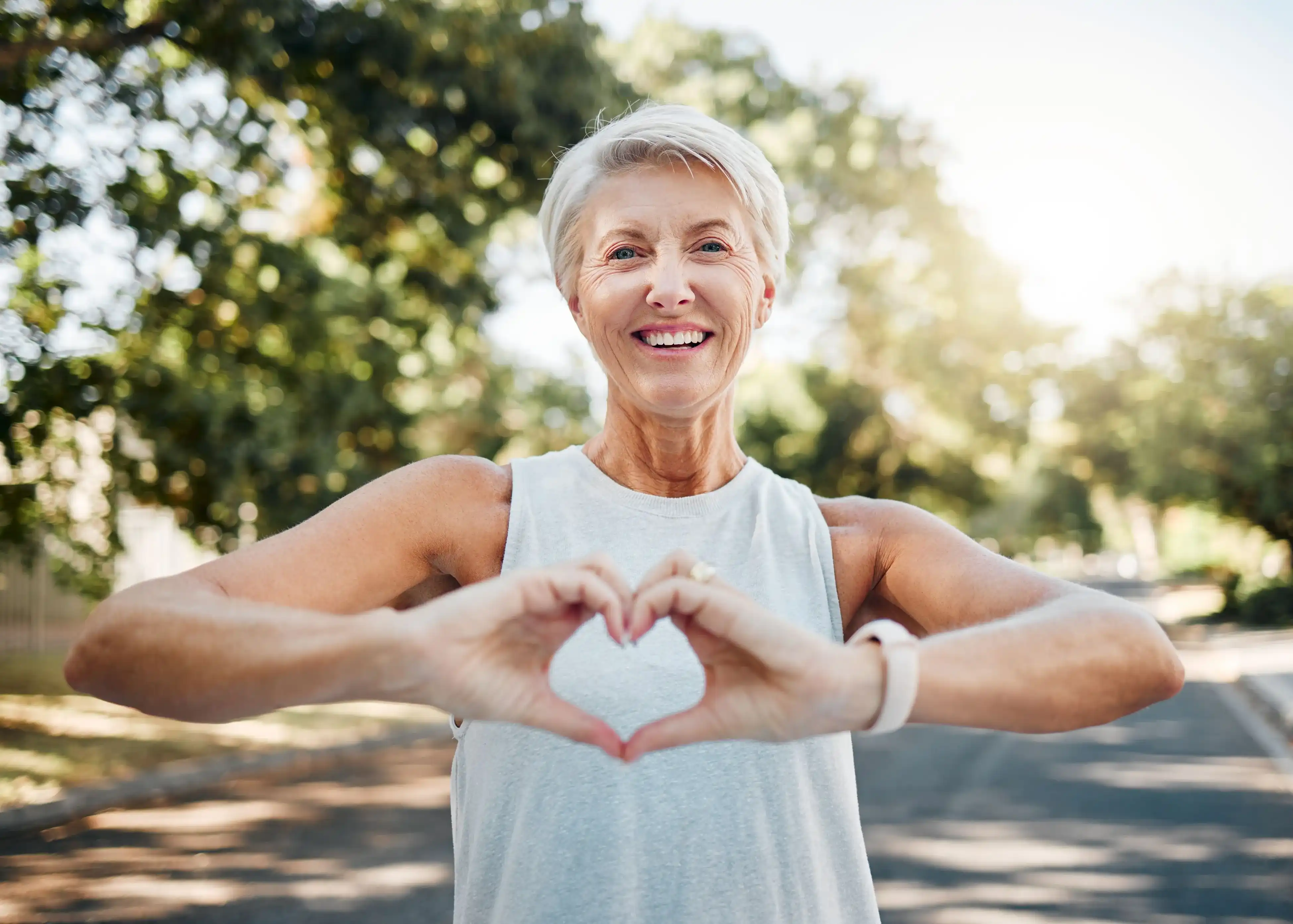 Smiling senior woman outdoors making a heart shape with her hands.
